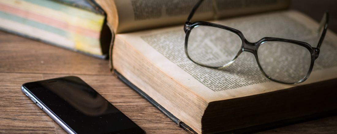 Foto von Büchern, auf denen eine Brille liegt. Auf der linken Seite liegt ein Smartphone.