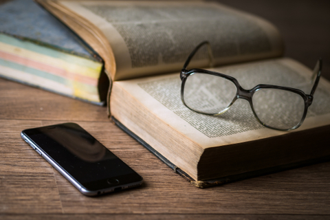 Foto von Büchern, auf denen eine Brille liegt. Auf der linken Seite liegt ein Smartphone.